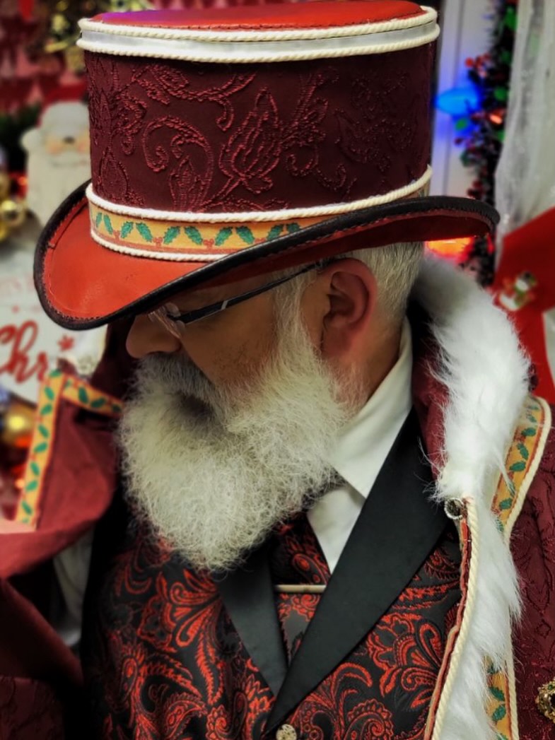 Saint Rick in his full Victorian Father Christmas attire — dark crimson coat, white beard, and top hat